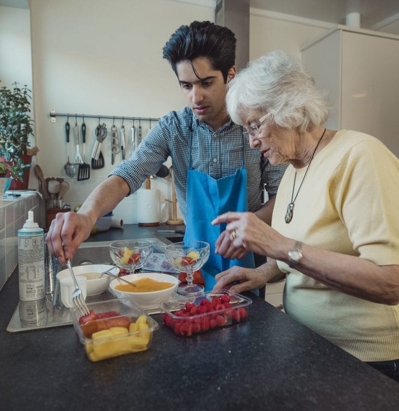 Teenage boy making fruit compote with his grandmother in the kitchen of her home.